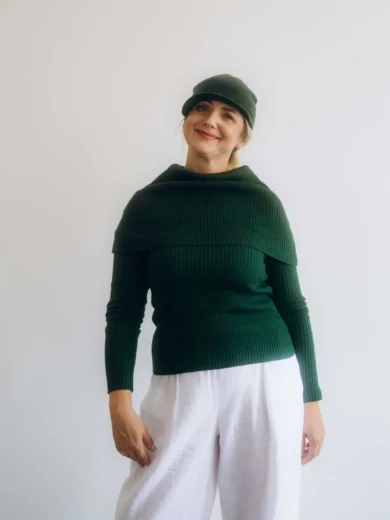 Dámske oblečenie štvorset TATTJA tmavozelený na modelke, elegantný pletený komplet s čiapkou, nákrčníkom a rukávnikmi v prírodnom odtieni zelenej.