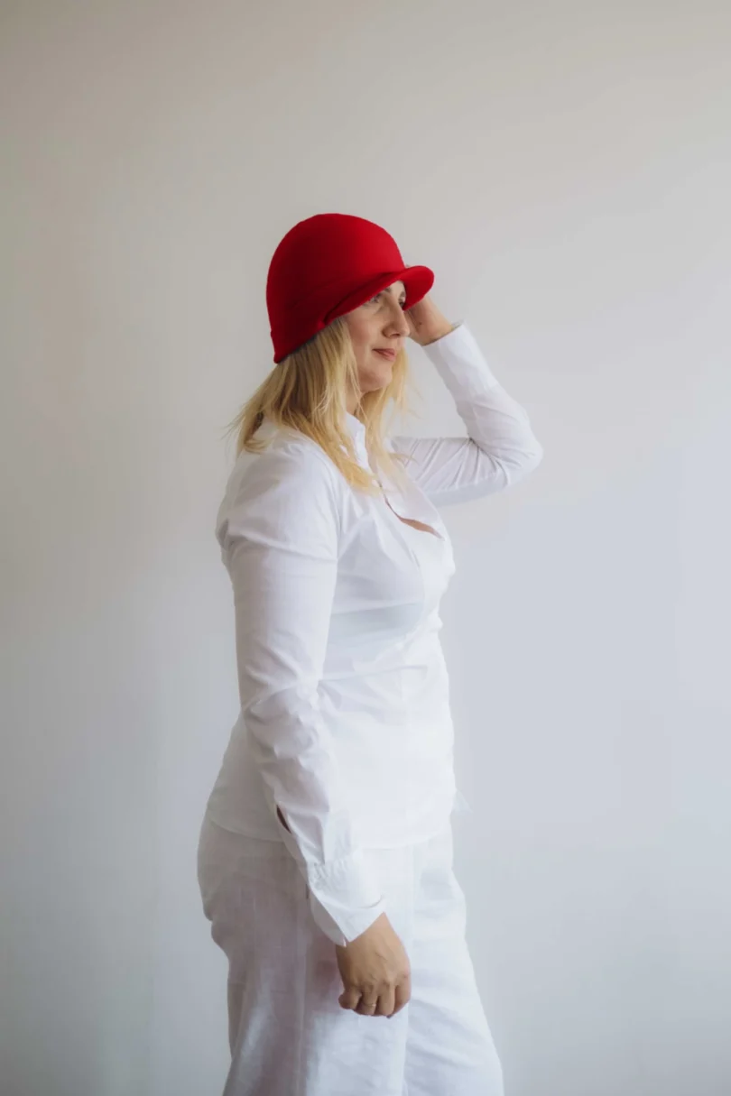 Modelka v bielom outfite TATTJA s červenou pletenou čiapkou ANJA, pohľad zboku