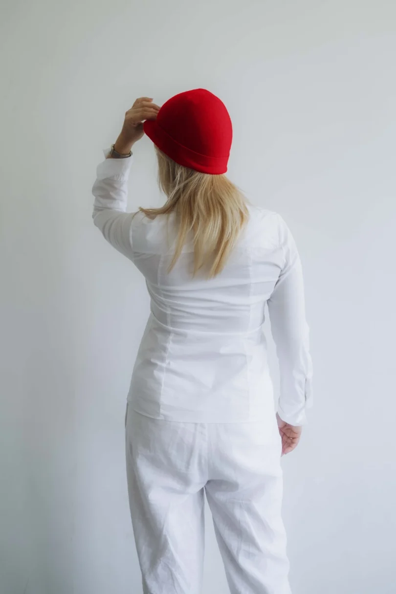 Modelka v bielom outfite TATTJA s červenou pletenou čiapkou ANJA, pohľad zozadu