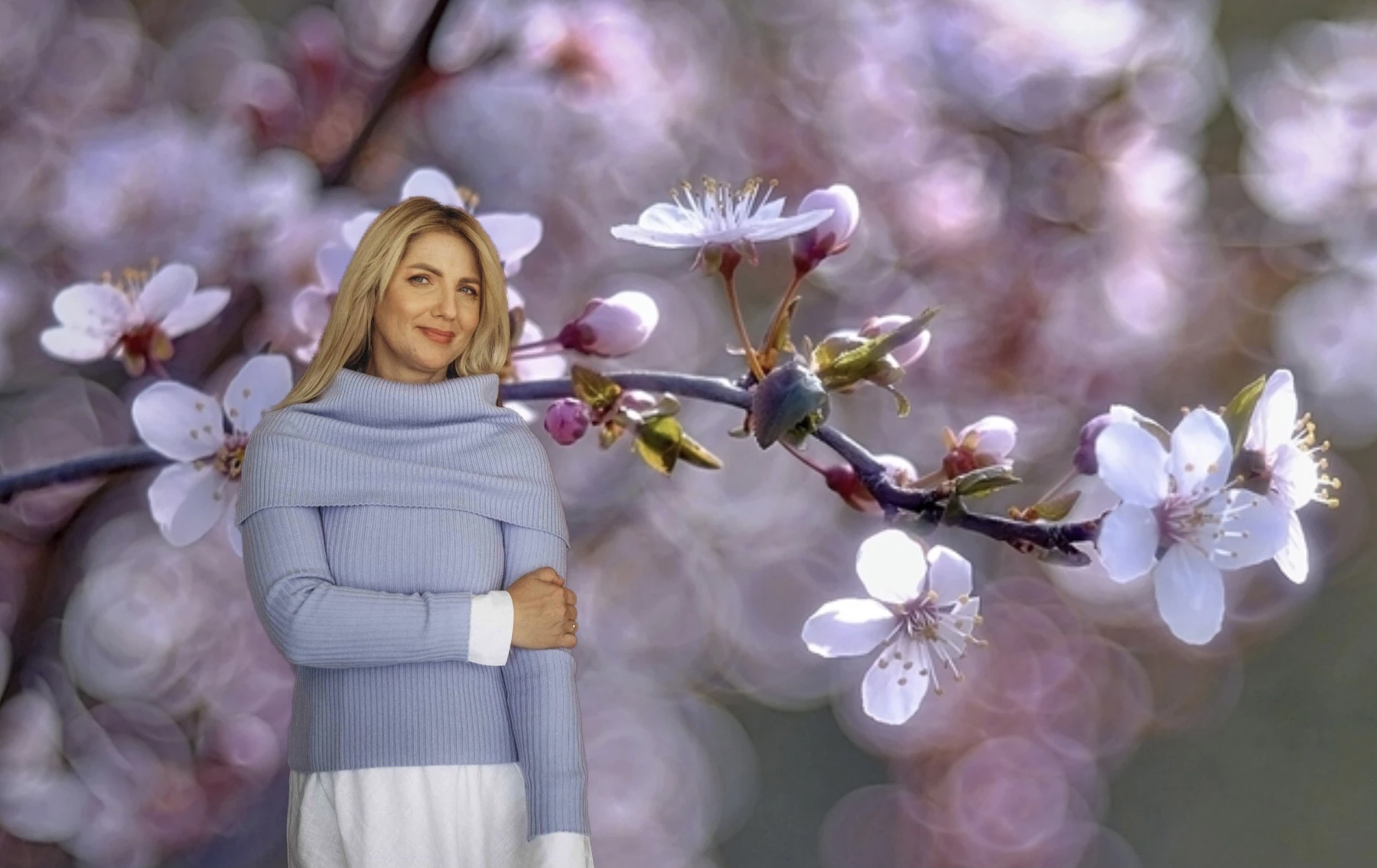Woman wearing light blue knit accessories styled for a spring walk, standing in front of blooming tree branches with soft pastel flowers.